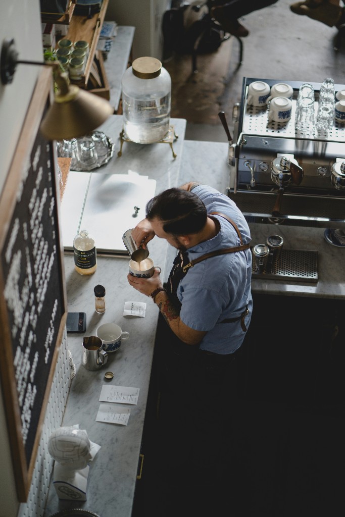 Barista pouring latte art behind a cafe counter